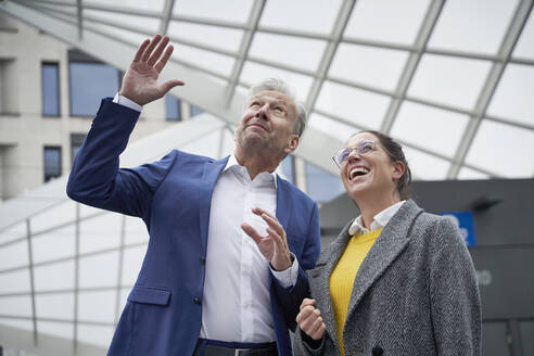 Businessman gesturing to cheerful female colleague while looking up in city - SDAHF01075