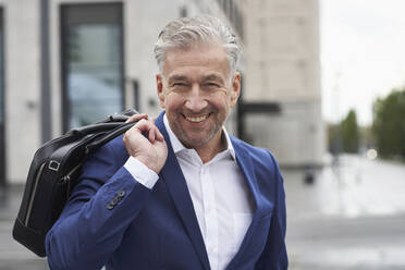 Smiling senior male entrepreneur holding laptop in city - SDAHF01081