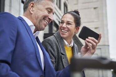 Cheerful businesswoman looking at senior male colleague sharing smart phone - SDAHF01100