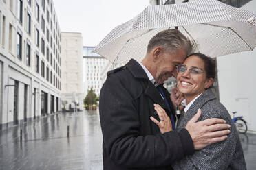 Glückliches Geschäftspaar unter Regenschirm in der Stadt während der Regenzeit - SDAHF01105