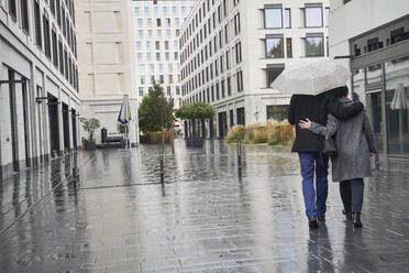 Geschäftsfrau und älterer Geschäftsmann, die sich unter einem Regenschirm in der Stadt während der Regenzeit umarmen - SDAHF01110