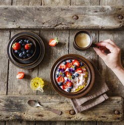 Female hand reaching for cup of coffee standing beside plate of quark with fruits and edible flowers - EVGF03851