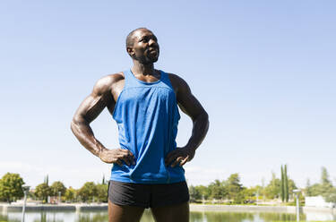 Sportsman with hand on hip looking away against clear sky in park - JCCMF00421