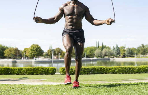 African male athlete doing skipping exercise in park on sunny day - JCCMF00425