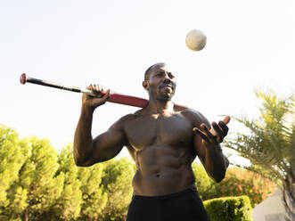 Männlicher Sportler mit Baseball im Park an einem sonnigen Tag - JCCMF00444