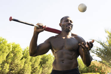 Männlicher Sportler mit Baseball im Park gegen klaren Himmel - JCCMF00448