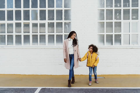 Mother and daughter holding hands while walking on road against building stock photo