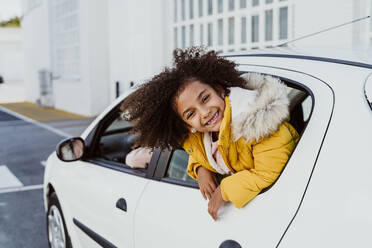 Cheerful girl peeking through window while traveling in car - EBBF01985