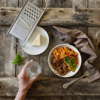 Schüssel mit vegetarischen Spaghetti Bolognese und Hand einer Frau, die ein Glas Wasser hält - EVGF03871