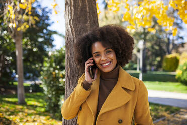 Lächelnde Frau, die im Park steht und mit ihrem Handy telefoniert - MRRF00732