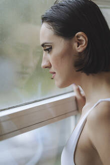Nahaufnahme einer nachdenklichen jungen Frau, die durch ein Fenster im Ballettstudio schaut - MTBF00824