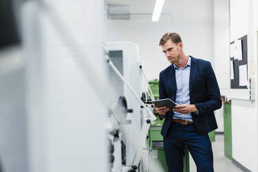 Businessman holding digital tablet while examining manufacturing equipment in industry - DIGF13773