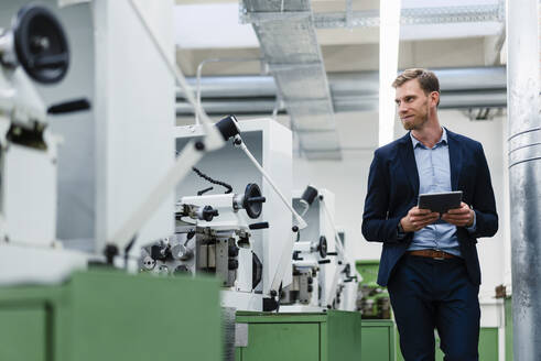 Lächelnder männlicher Fachmann mit digitalem Tablet, der sich beim Gehen in einer Fabrik umsieht - DIGF13774