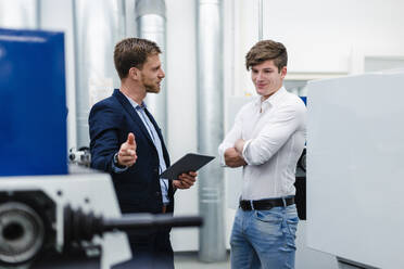 Male coworkers with digital tablet talking about machines while standing in industry - DIGF13779