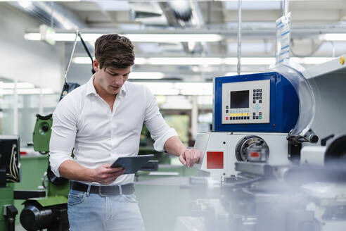 Männlicher Fachmann, der ein digitales Tablet benutzt, während er an einem Maschinenpark in der Industrie steht - DIGF13784