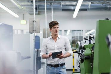 Selbstbewusster männlicher Ingenieur, der ein digitales Tablet hält, während er in einer Fabrik spazieren geht - DIGF13788