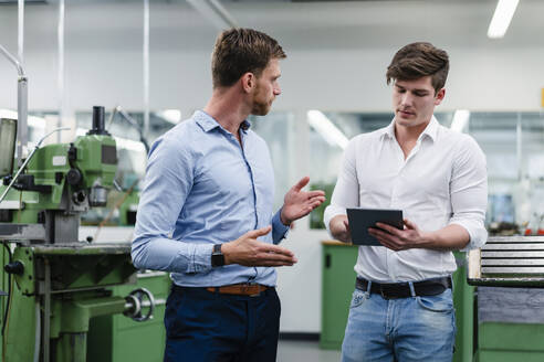 Männlicher Unternehmer im Gespräch mit einem Ingenieur bei der Arbeit an einem digitalen Tablet in einer Fabrik - DIGF13789