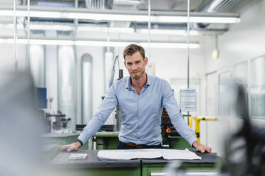 Smiling male entrepreneur with floor plan in industry - DIGF13798