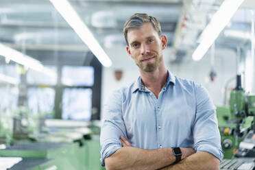 Smiling businessman with arms crossed standing in industry - DIGF13803