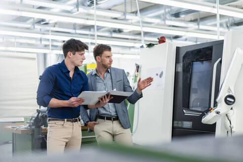 Geschäftsmann erklärt männlichen Ingenieur mit Datei Dokument über die Herstellung in der Fabrik - DIGF13811