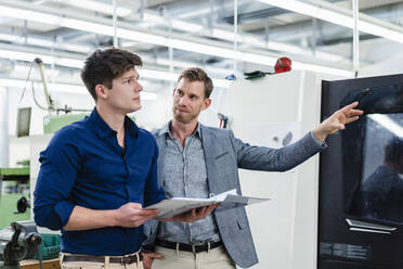 Männlicher Unternehmer, der einen Kollegen ansieht, während er über die Maschinenausstattung in der Industrie diskutiert - DIGF13813