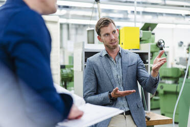 Männlicher Fachmann, der mit einem Ingenieur in einer Fabrik über Produktionsanlagen spricht - DIGF13814