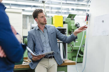 Male entrepreneur with file document discussing over machinery equipment with colleague in factory - DIGF13817