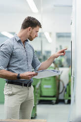 Male engineer holding file document while operating manufacturing equipment in industry - DIGF13844