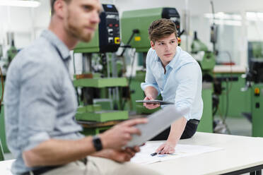Male engineer holding digital tablet with entrepreneur looking away while having meeting in factory - DIGF13849