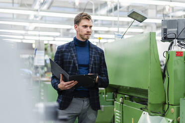 Geschäftsmann, der ein Dokument in der Hand hält und die Maschinenausrüstung in einer Fabrik untersucht - DIGF13855