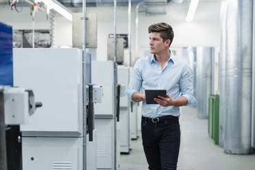 Male professional with digital tablet looking around while walking in industry - DIGF13860