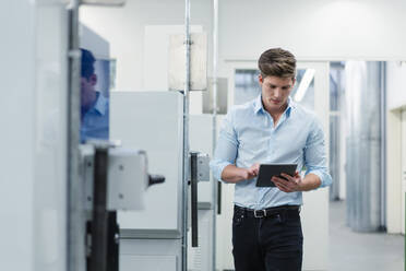 Male entrepreneur working on digital tablet while walking by machines in factory - DIGF13861