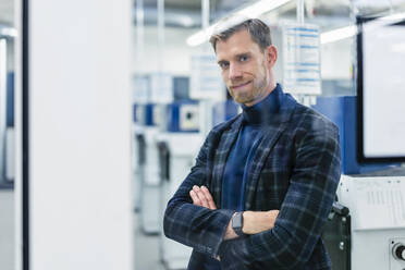 Smiling male professional with arms crossed standing in factory - DIGF13863