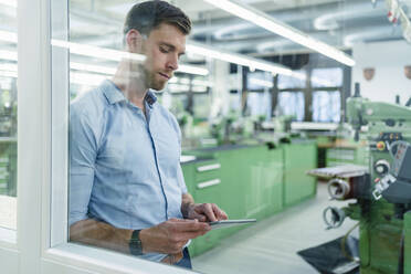 Mid adult businessman working on digital tablet seen through glass in industry - DIGF13884