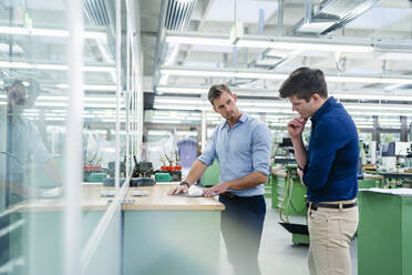 Male coworkers discussing over digital tablet on desk while working in factory - DIGF13887