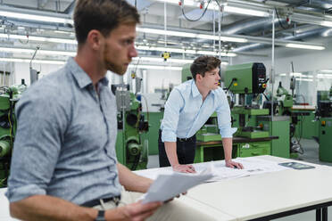 Businessman looking away while standing with male colleague in industry - DIGF13906