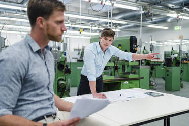 Businessman pointing while discussing with male colleague in factory - DIGF13907