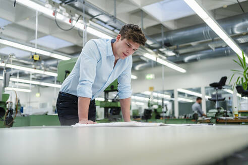 Geschäftsmann, der eine Blaupause am Schreibtisch in der Industrie prüft - DIGF13912