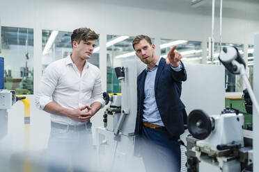 Businessman pointing while explaining male colleague about machinery in factory - DIGF13920