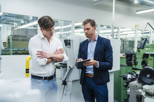 Geschäftsmann diskutiert mit einem männlichen Mitarbeiter über ein digitales Tablet in einer Fabrik - DIGF13921