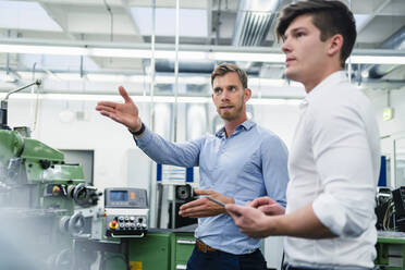 Businessman explaining male coworker about machinery in factory - DIGF13928