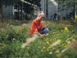 Smiling businesswoman looking at flowers in company garden - GUSF04854