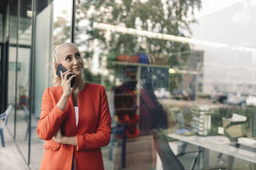 Weibliche Unternehmerin spricht mit einem Smartphone vor einem Bürogebäude - GUSF04878