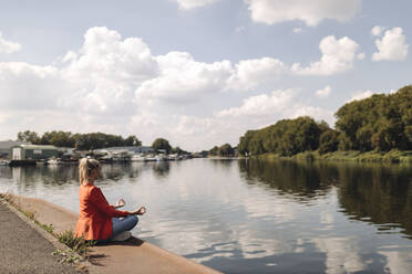 Businesswoman meditating at lakeshore against sky - GUSF04886