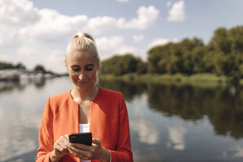 Eine Unternehmerin benutzt ihr Smartphone an einem sonnigen Tag am See - GUSF04887