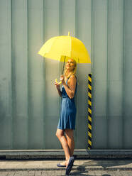 Young woman with umbrella on footpath against wall during sunny day - GUSF04900