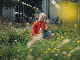 Happy female entrepreneur with digital tablet in office garden - GUSF04907