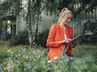 Young businesswoman using digital tablet while sitting in office garden - GUSF04910