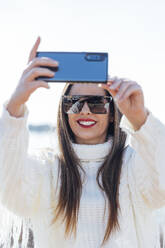 Nahaufnahme einer schönen Frau mit Sonnenbrille, die ein Selfie gegen den klaren Himmel macht - JRVF00079