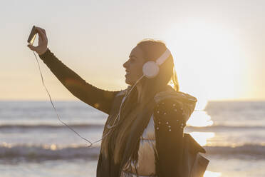 Schöne Frau, die Selfie beim Hören von Musik gegen das Meer bei Sonnenuntergang - JRVF00084